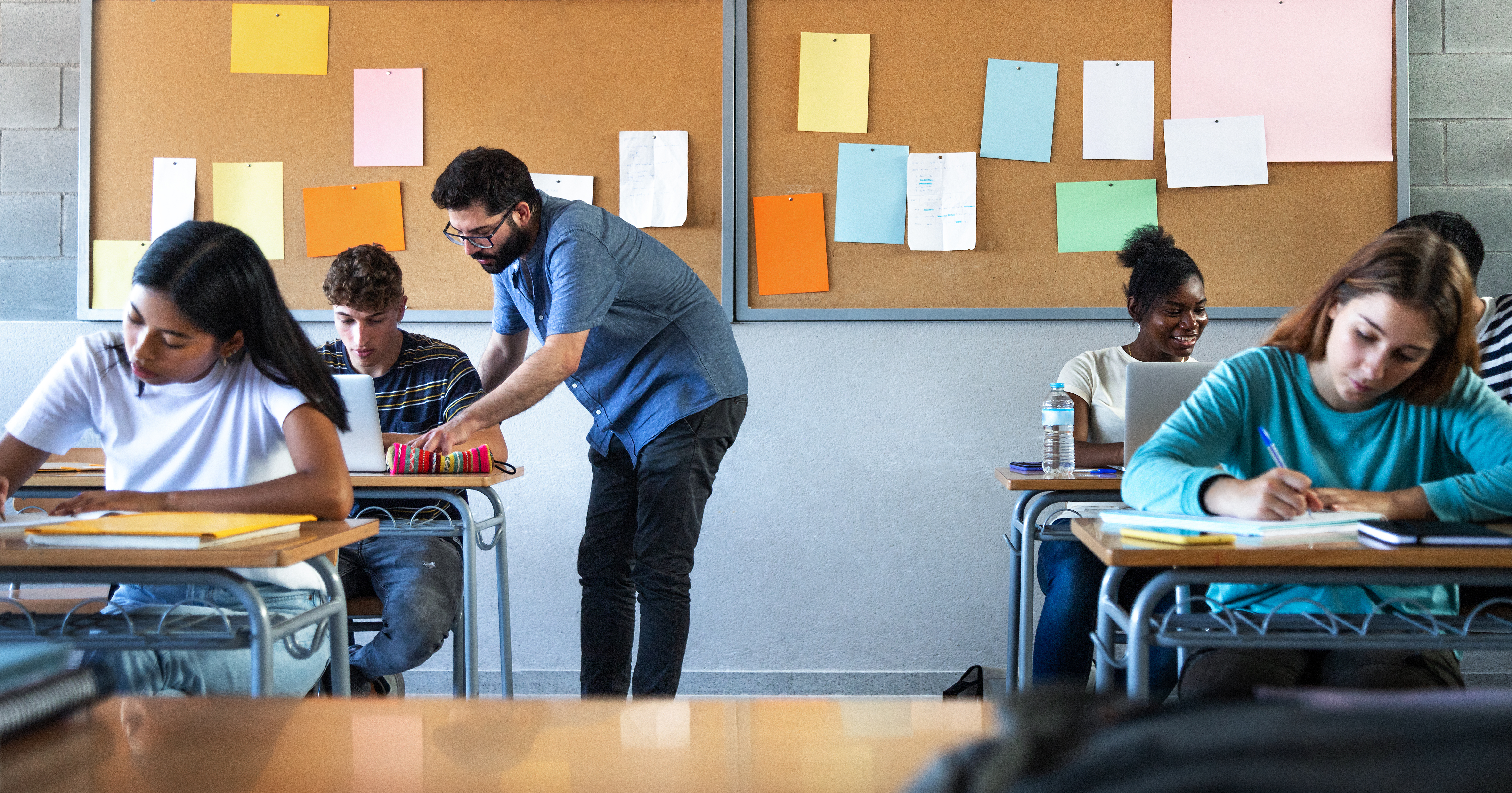 male teacher hovering over a students desk in a classroom