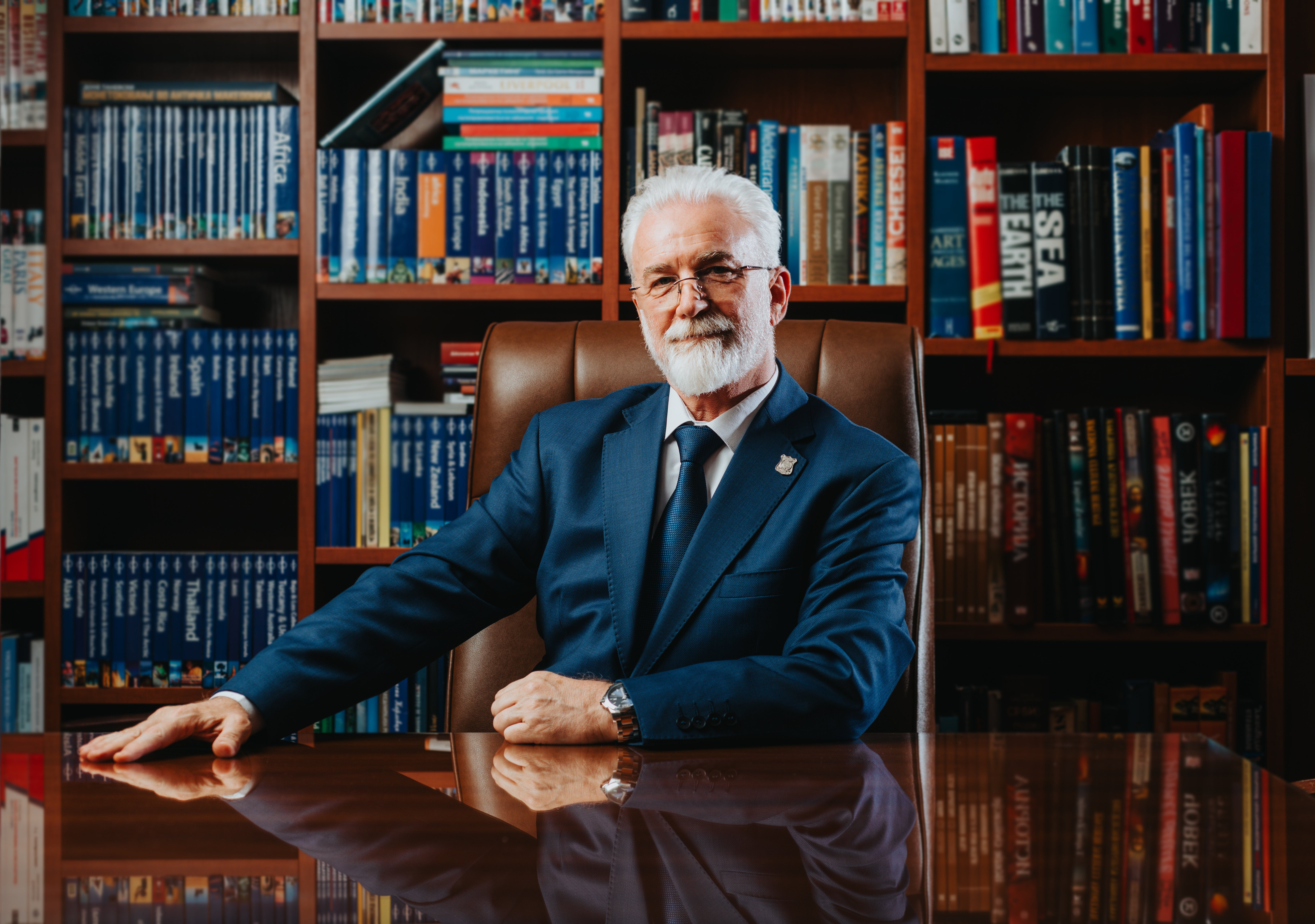 Caucasian university rector in 60s or 70s, poses confidently in a book-filled library. Mature professor exudes wisdom as experienced leader of academia, overseeing successful school.