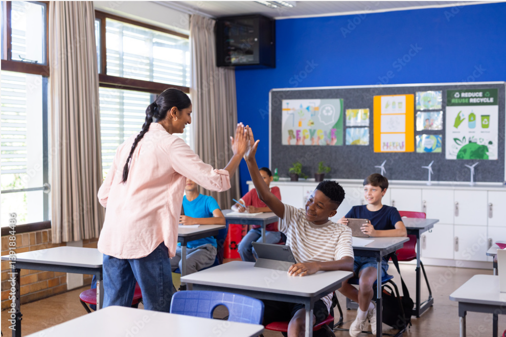 In school, Indian female teacher giving high-five to student using tablet in classroom