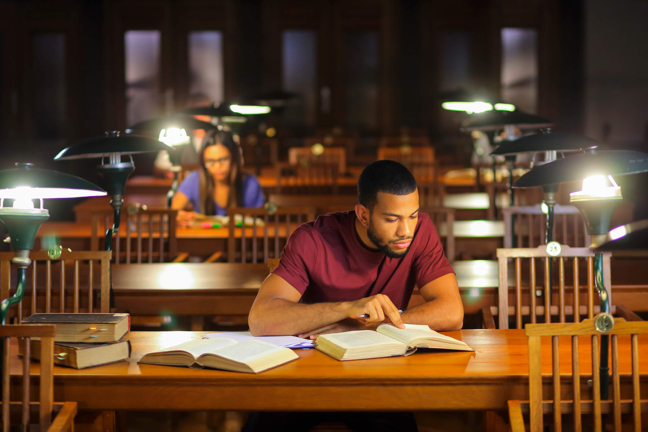 Man sits at a library table researching several books.